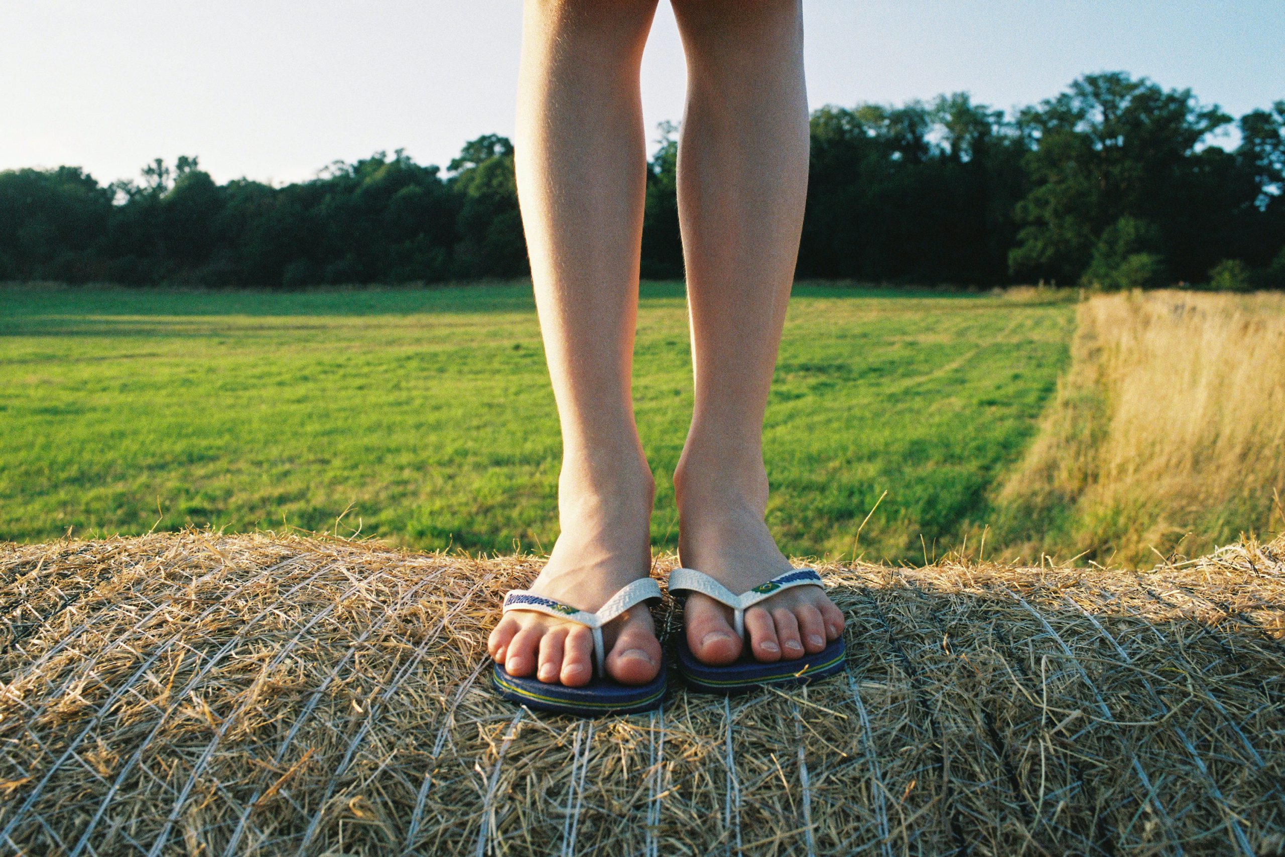 person wearing black flip flops standing on brown grass field during daytime